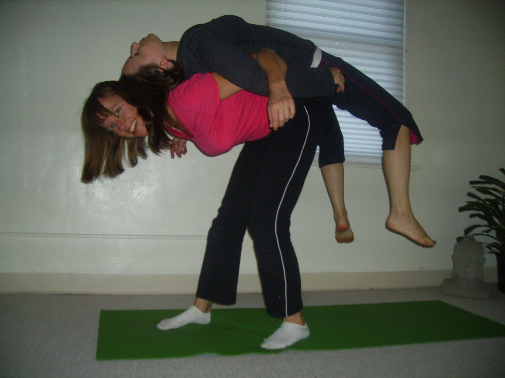 Standing Backbend. Line up the tailbone first.  Step into your 'power stance' position.  Keep your bodies relaxed and slowly ask your partner to roll onto your back.  When they are comfortable raise them off the ground. This is a great LAUGH!..