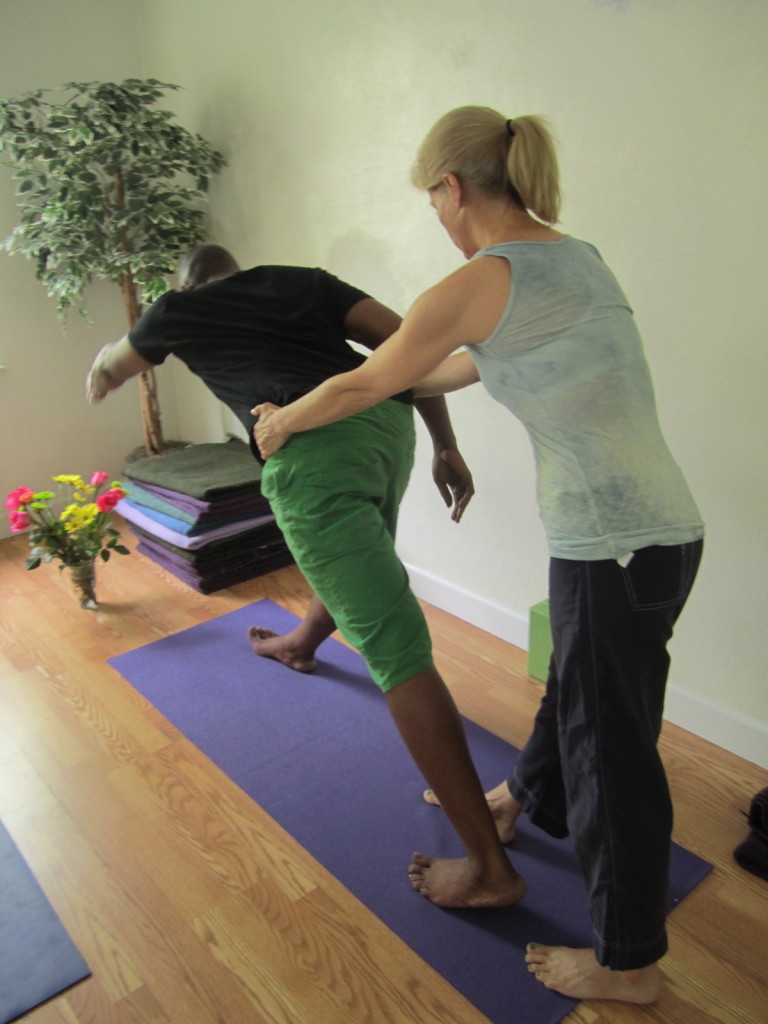 A partner assisted forward fold Parsvatanasana.  Pull back greatly on your partner hips, at the same time, having them lean forward and feel the balance between the left and right hip.  This is amazing for your hips and can often strengthen hidden weak spots and offset problems down the road. Notice the back heel is still elevated above the floor.  Also, the spine is free as a bird to lengthen and massage the internal organs generating more of the relaxation or parasympathetic response in the brain.