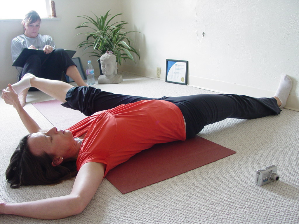 Reclining Supta Pandangusthasana Pose with the assist of the wall.  We include this pose to demonstrate the importance of dropping the back thigh into the earth and lengthening out through the flexion and foot.  The wall gives the leg an active reminder to work from  the base of the foot rather than the head or brute force.  Taking the leg out to the side, we keep the hips leveled and feel vital energy move through the body. A great way to prepare for the standing pose next.